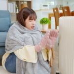 オイルヒータの前で寒がる女性