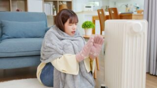 オイルヒータの前で寒がる女性